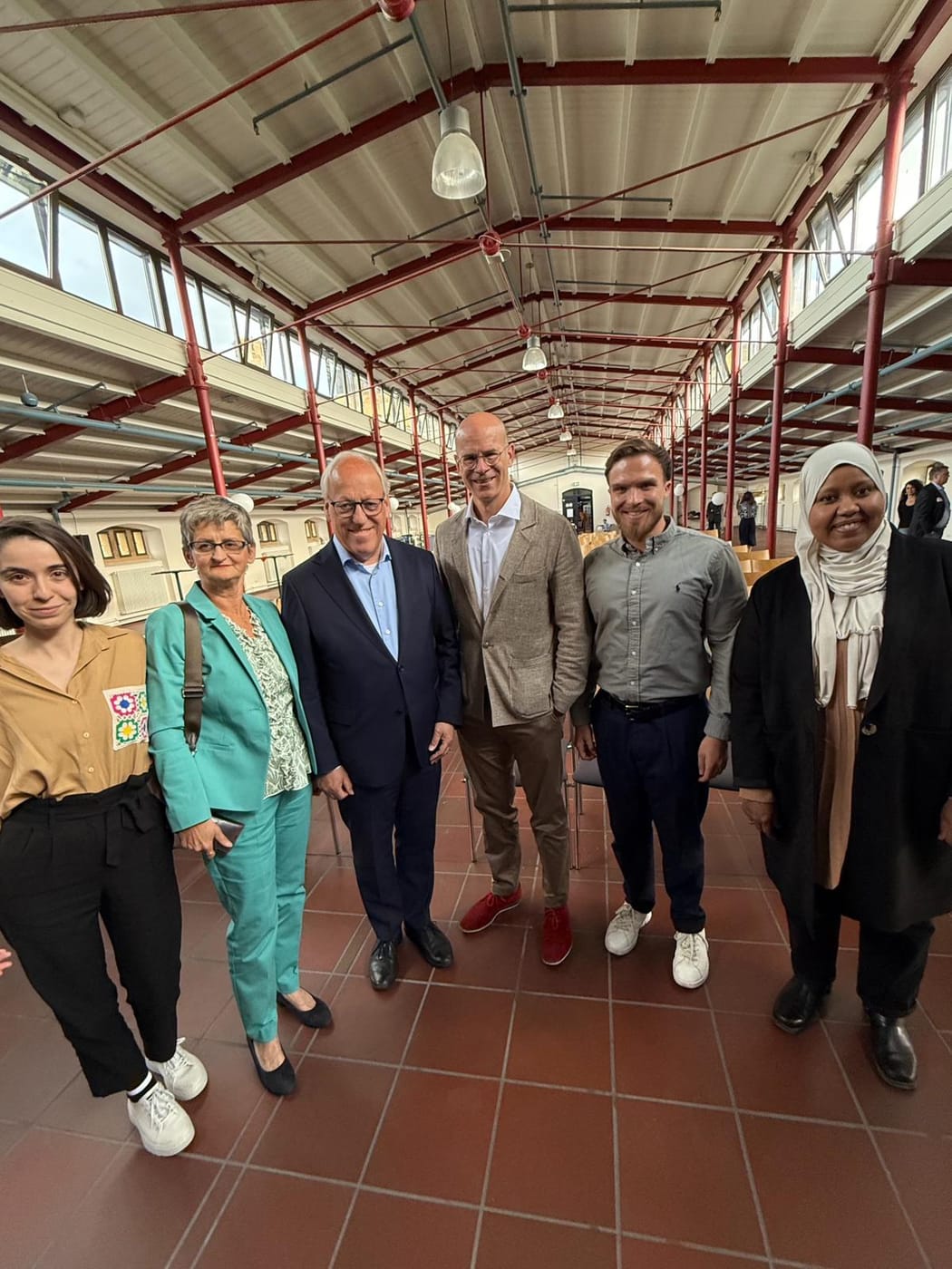 Gruppenfoto von Vertreterinnen und Vertretern des Ausschusses für Chancengerechtigkeit und Integration mit Gästen aus Politik und Verwaltung in einer historischen Industriehalle.